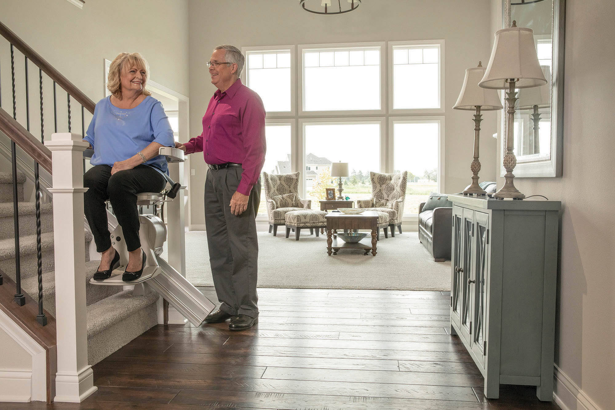 Woman using a stairlift at home with a family member beside her