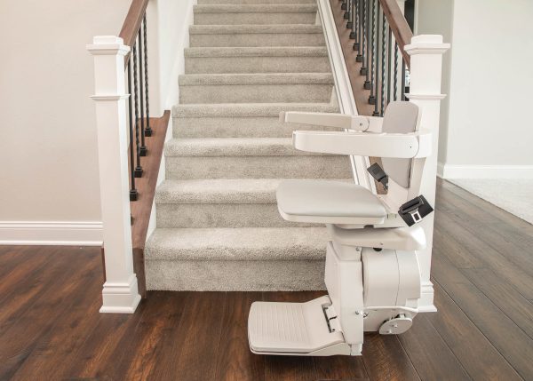 Straight rail stairlift parked at the bottom of a carpeted staircase