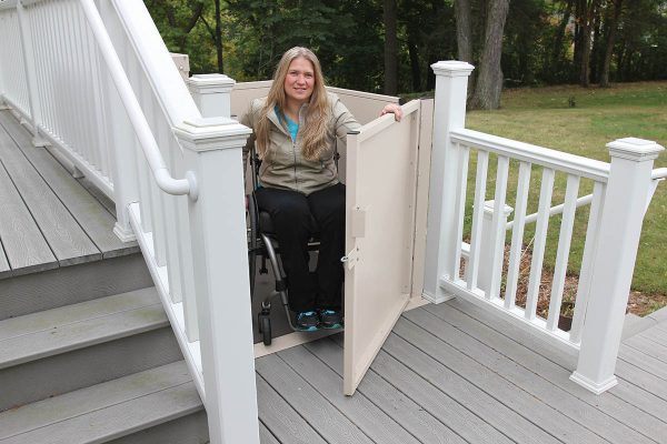 A woman in a wheelchair using a residential vertical platform lift at a home entrance