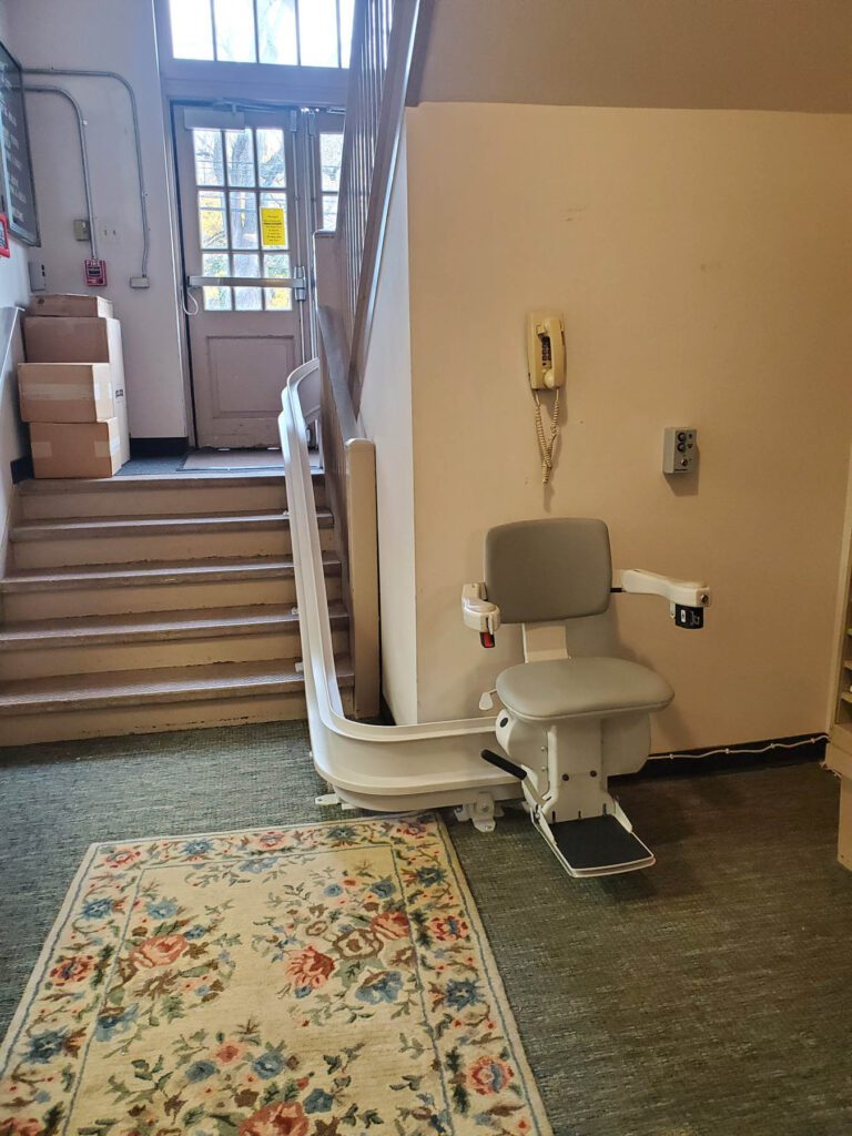 A curved stairlift at the bottom of a stairwell beside the entrance door of a community building